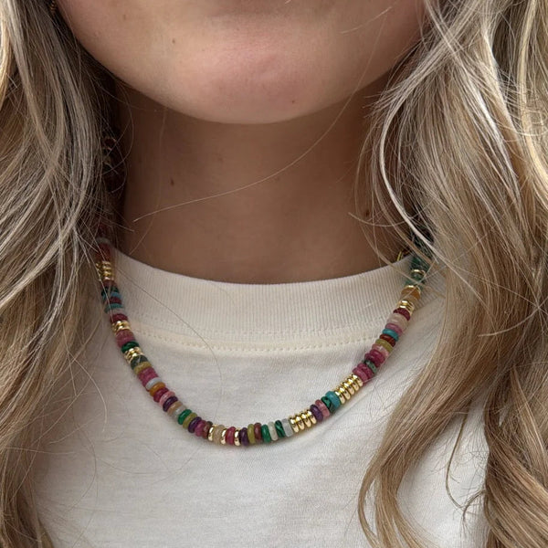 A close-up of a person wearing a short beaded necklace with multicolored round beads, paired with a cream-colored t-shirt featuring a pink starfish graphic.