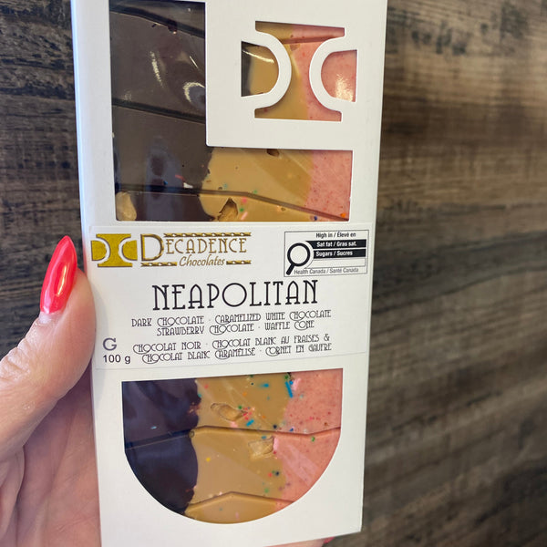Hand holding a box of Neapolitan ice cream with visible brand name on a wooden surface