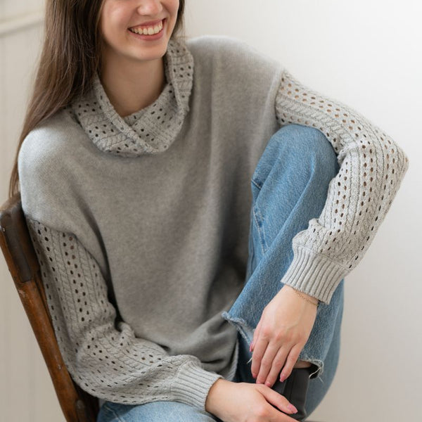Woman wearing a gray sweater with lace sleeves sitting on a chair.