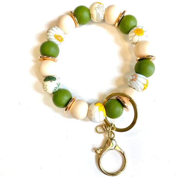 A beaded keychain bracelet featuring matte green and cream beads, some with white daisy floral patterns, accented by gold-toned metal spacers and a lobster clasp.