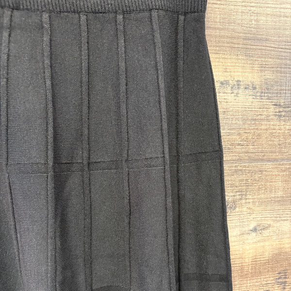 Close up of a black knit skirt, elastic waist, horizontal and vertical knit pattern, mid length.