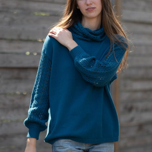Woman wearing a blue knitted sweater standing against a wooden wall.