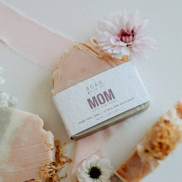 Bar of soap with a 'Mom' label surrounded by flowers on a marble surface