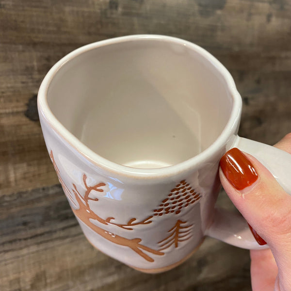 Ceramic mug with decorative design held by a hand on a wooden surface