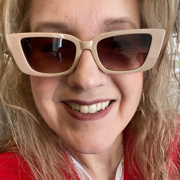 Close-up of a person wearing beige sunglasses with a red garment in the background