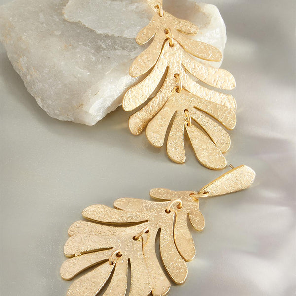 Gold leaf-shaped earrings on a textured surface
