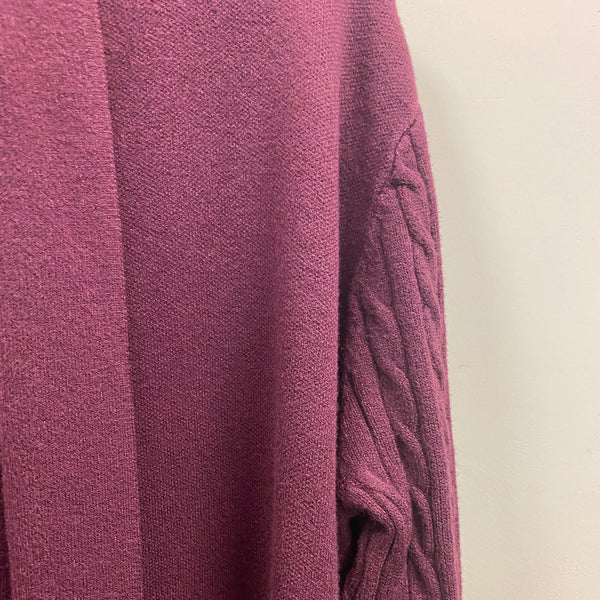 A close-up of a textured knit sweater in a dusty plum purple color, showing a smooth section and a cable-knit sleeve detail against a plain off-white background.