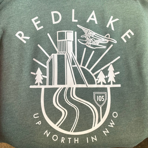 A dark green heathered t-shirt featuring a white graphic print of a red lake scene with an airplane, trees, a bridge, and the text 'REDLAKE UP NORTH IN NWO' and '105'.