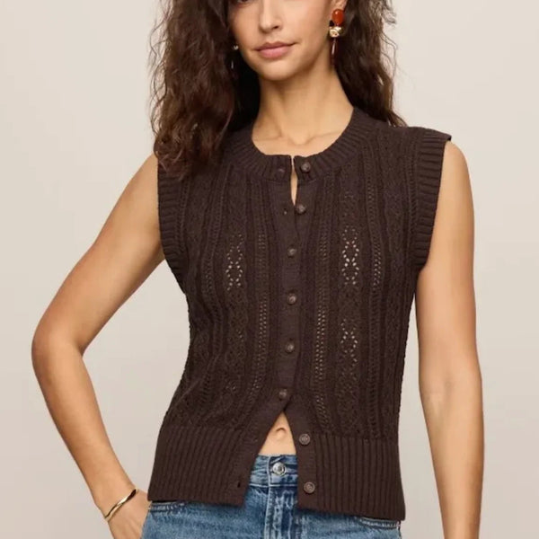 A woman modeling a sleeveless dark brown knit button-front vest with textured cable and openwork details, paired with blue jeans against a plain light beige studio background.