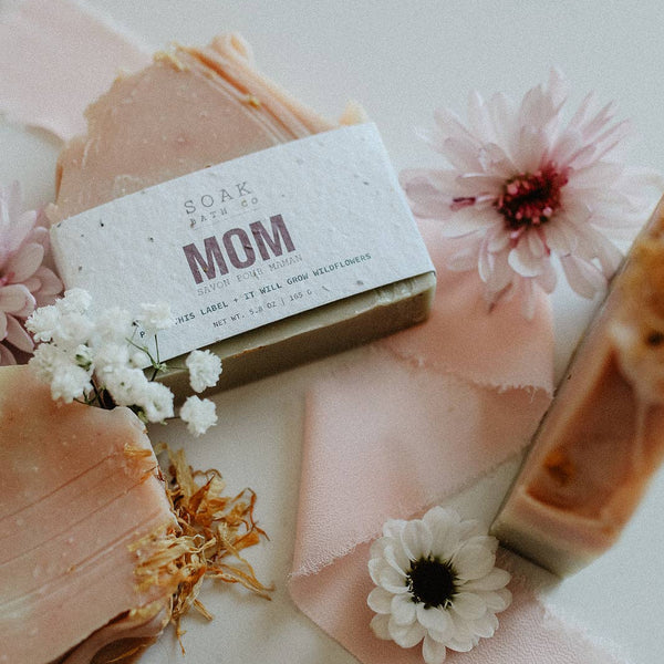Bar of soap with 'Mom' label surrounded by flowers on a light background