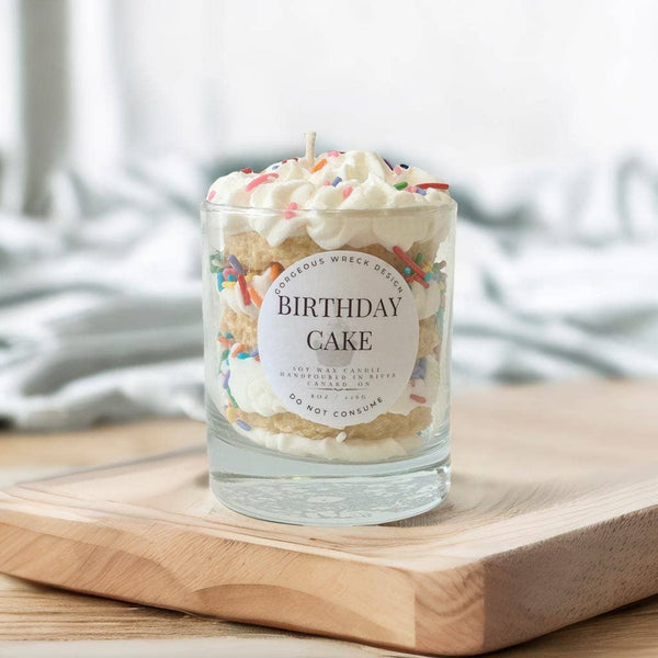 Glass candle with birthday cake design and 'Birthday Cake' label on a wooden surface.