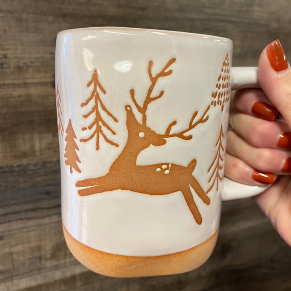Mug with deer design held by a hand on a wooden surface