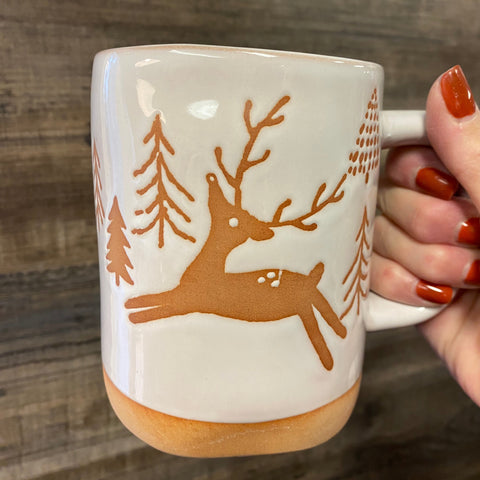 Mug with deer design held by a hand on a wooden surface