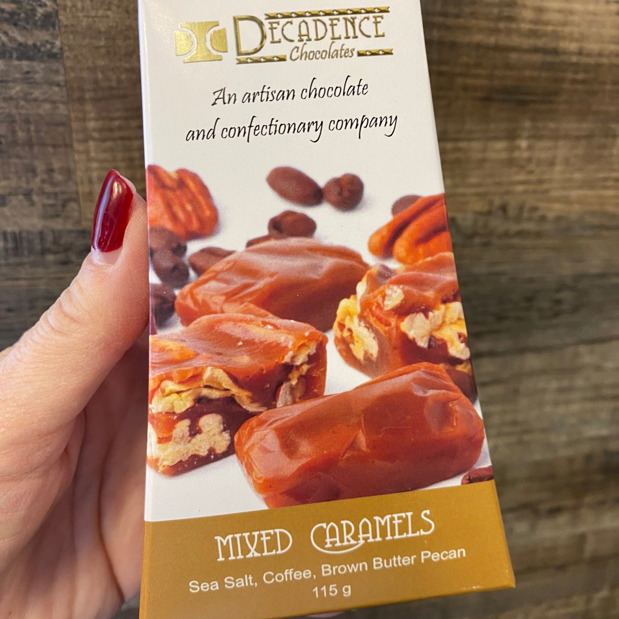 Decadence Mixed Caramels packaging held by a hand on a wooden surface