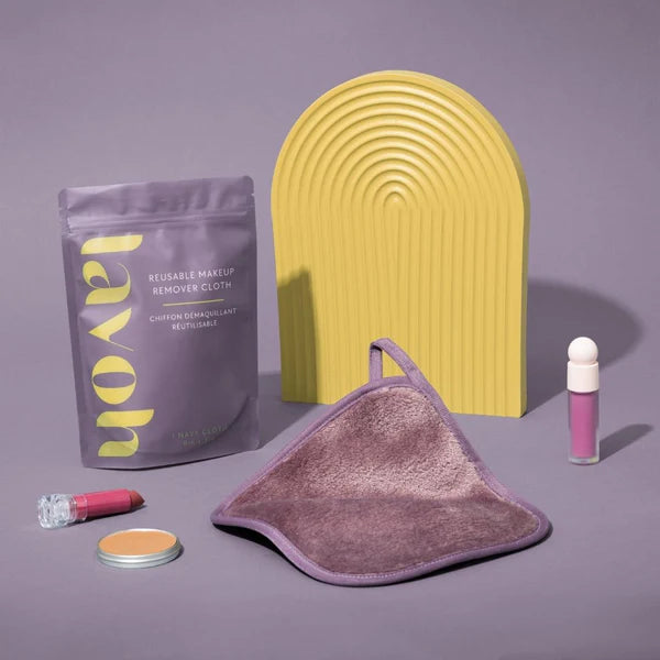 Makeup removal products including a purple package, yellow tool, and pink bottle on a gray background