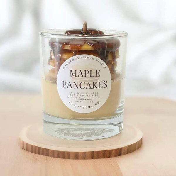 Candle labeled 'Maple Pancakes' on a wooden stand with a light background