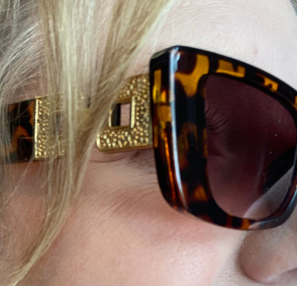 Close-up of a person wearing tortoiseshell sunglasses with a gold clip-on accessory.