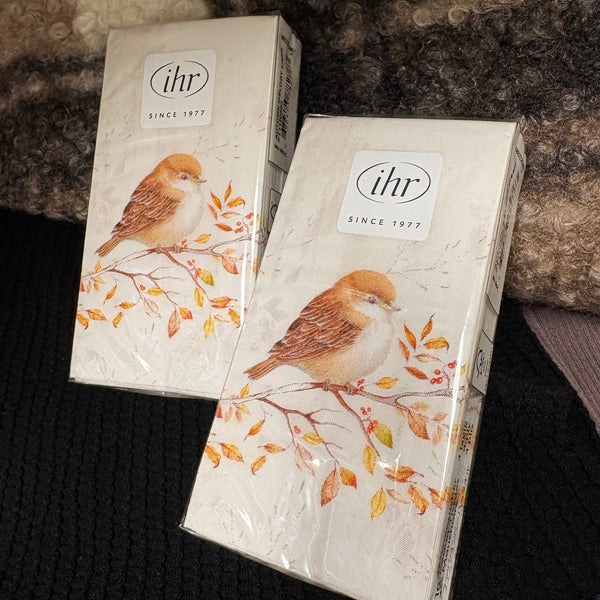 Two rectangular paper product boxes with a bird illustration and the visible brand mark 'ihr SINCE 1977' placed on a dark textured surface with a fuzzy brown blanket behind them.