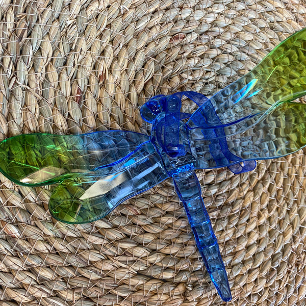 Blue and green plastic dragonfly toy on a woven mat