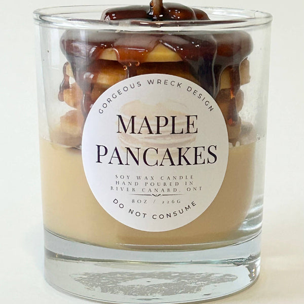 Candle in a glass jar labeled 'Maple Pancakes' with a decorative top on a white background.