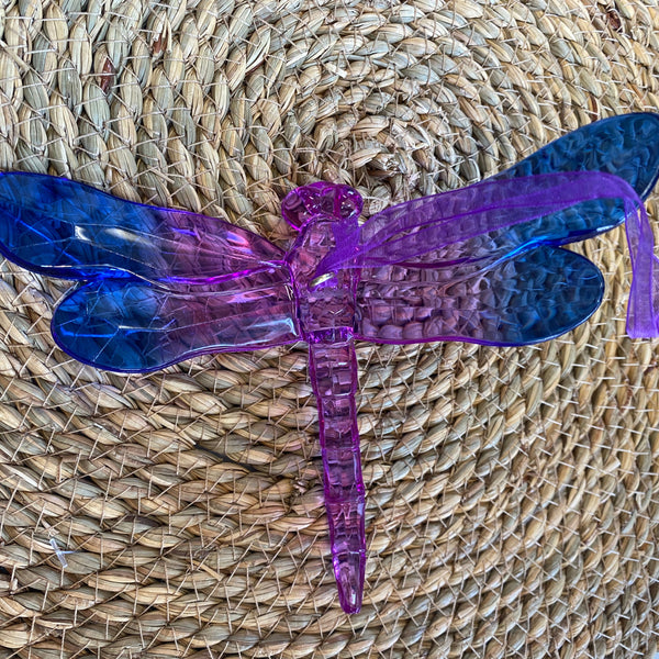 Translucent purple and blue dragonfly-shaped object on a woven mat