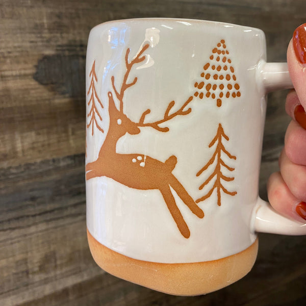 Mug with brown tree design held by a hand on a wooden surface