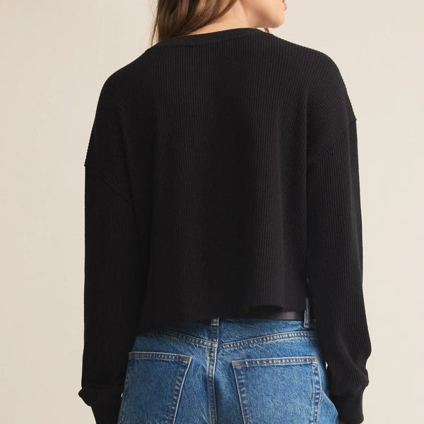 Person wearing a black sweater and blue jeans on a beige background