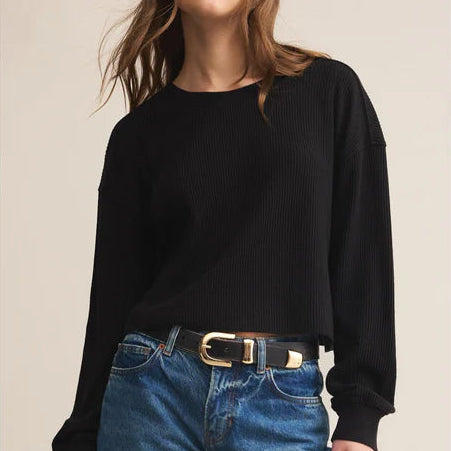Woman wearing a black sweater and blue jeans with a beige background