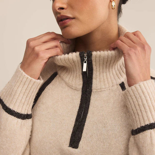 Woman wearing a beige sweater with black trim on a neutral background