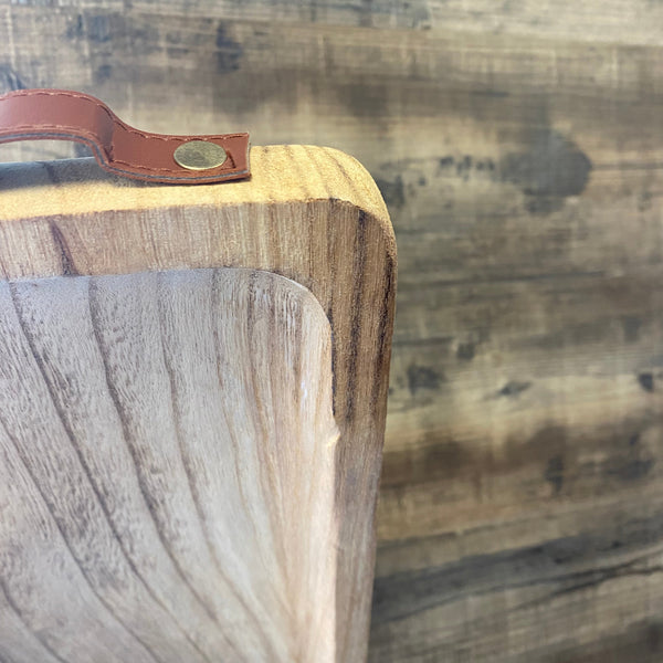 Wooden cutting board with a leather handle on a wooden surface
