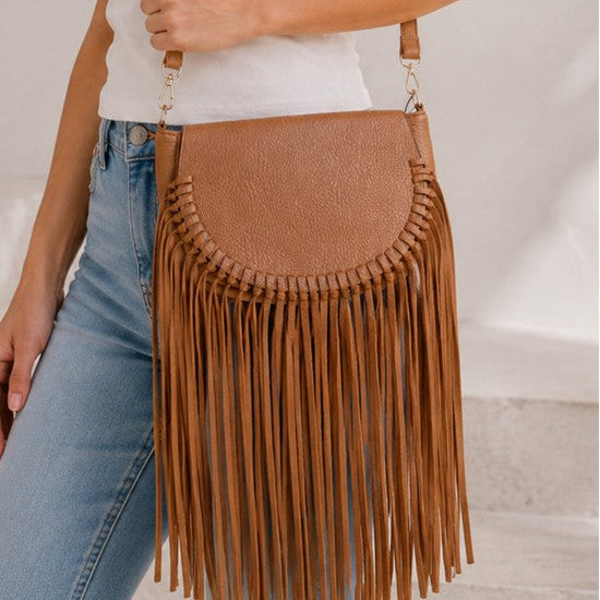 Brown fringed handbag held by a person wearing a white top and blue jeans.