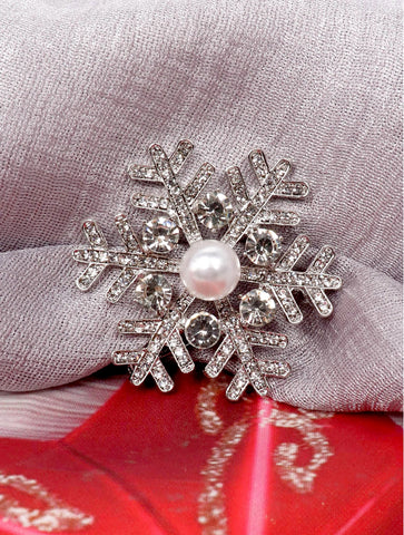 Silver snowflake brooch with a pearl center on a red and gray fabric background