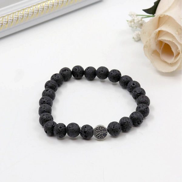 Black beaded bracelet with a silver clasp on a white surface with a rose and mirror in the background.