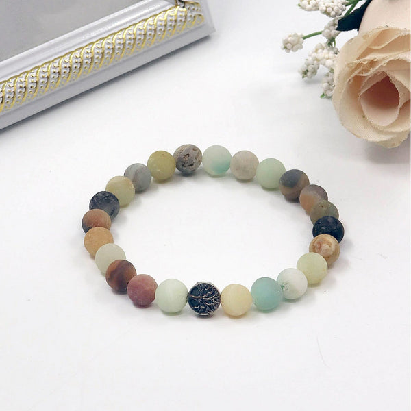 Multicolored beaded bracelet on a white surface with a decorative frame and flowers in the background.