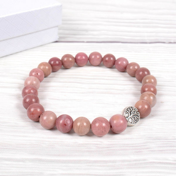 Pink beaded bracelet with a silver tree of life charm on a white background