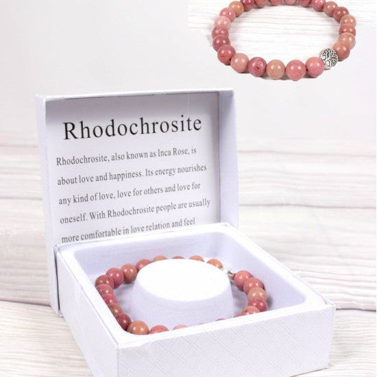 Pink rhodochrosite bracelet in a white box with information card on a light wooden surface