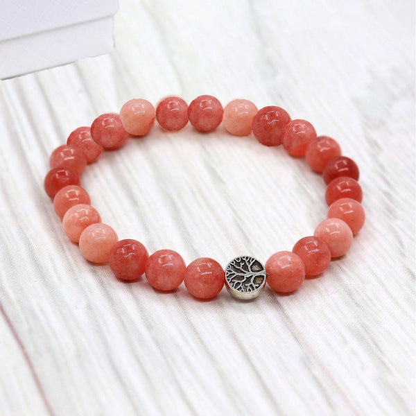 Pink beaded bracelet with a silver tree charm on a white wooden surface