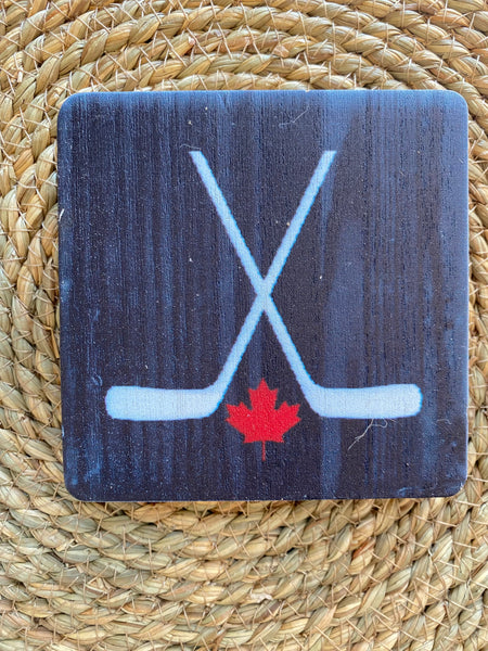 Coaster with hockey sticks and a red maple leaf on a blue background, placed on a woven mat.