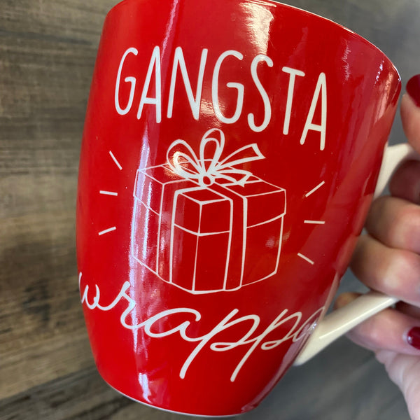 Red mug with white text and design held by a hand on a wooden surface