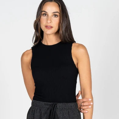 A woman modeling a sleeveless black ribbed knit top paired with dark gray drawstring sweatpants against a light gray studio background.