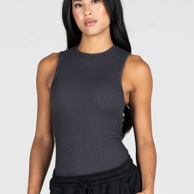A woman modeling a dark gray ribbed sleeveless crop top paired with black drawstring sweatpants against a light gray studio background.