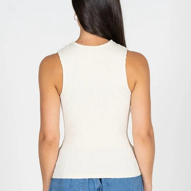 A woman viewed from the back wearing a ribbed sleeveless knit top in off-white and blue jeans, set against a plain light gray studio background.