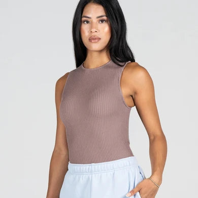 A woman modeling a sleeveless ribbed knit top in a muted taupe-brown color, paired with light blue sweatpants, against a solid light gray background.