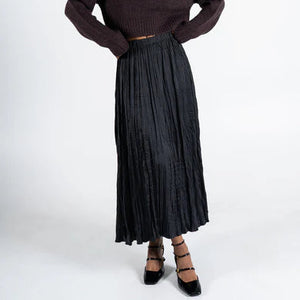 Woman wearing a brown sweater and black pleated skirt on a white background