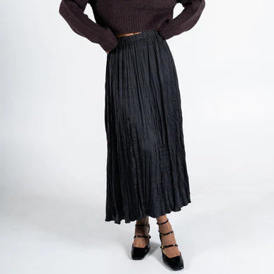 Woman wearing a brown sweater and black pleated skirt on a white background