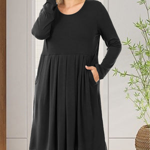 Black dress worn by a person with a white wall and plant in the background