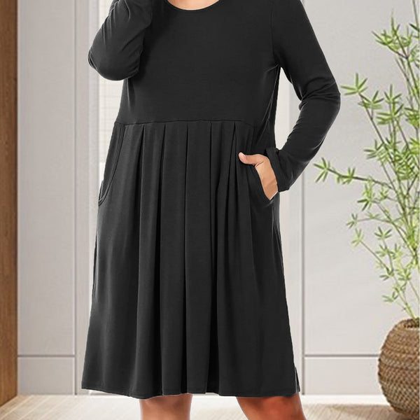 Woman wearing a black dress with long sleeves in a room with a plant.