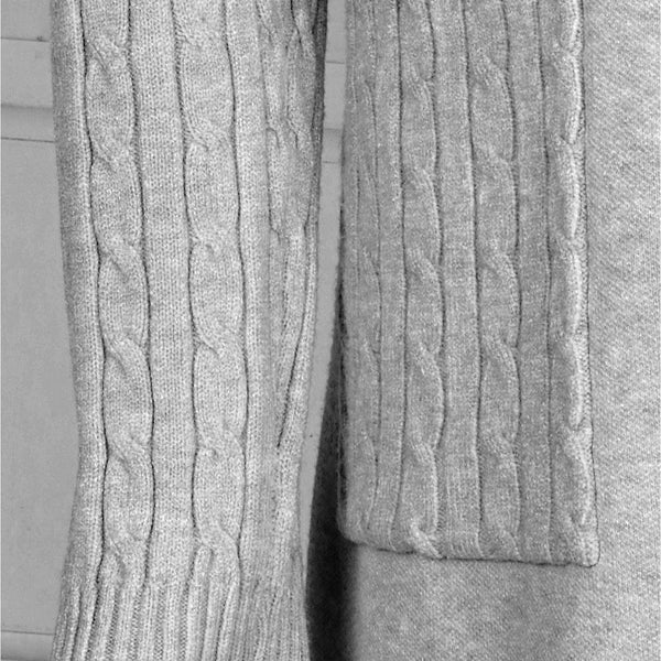 Close-up of a light gray cable-knit sweater showing the sleeve and a matching chest pocket with ribbed trim.