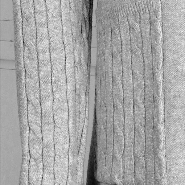 Close-up of a light gray cable-knit sweater showing the sleeve and a matching chest pocket with ribbed trim.