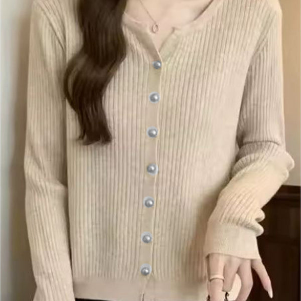 A woman wearing a beige ribbed knit cardigan with a split neckline and light blue buttons, paired with black bottoms and holding a chain strap.
